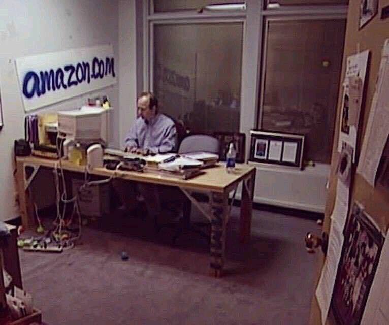 1999년, amazon.com 이라 손으로 쓴 간판이 있는 작은 사무실에 혼자 앉아 컴퓨터로 일을 하고 있는 제프 베조스